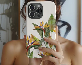 May include: A white phone case featuring a watercolor illustration of a bird of paradise flower with yellow, orange, and purple petals, and green leaves. The case is held in front of a person.