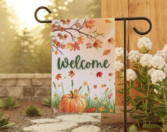 May include: A welcome garden flag with a fall theme. The flag features a pumpkin, leaves, and birds on a white background with the word "welcome" in green.
