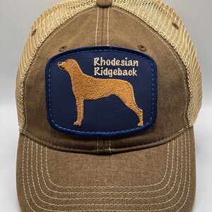 May include: Brown and tan trucker hat with a blue patch featuring a Rhodesian Ridgeback dog and the text "Rhodesian Ridgeback".