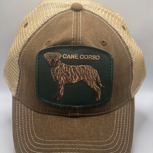 May include: Brown and beige trucker hat with a green patch featuring a brown Cane Corso dog silhouette and the text "Cane Corso".