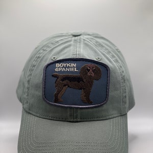 May include: A green baseball cap with an embroidered patch featuring a brown Boykin Spaniel dog and the text "Boykin Spaniel".