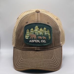 Op de afbeelding: Bruine en beige baseballcap met een mesh achterkant. De voorkant heeft een geborduurd embleem met een beer en twee welpen voor bomen, met de tekst "ASPEN, CO." in het wit.