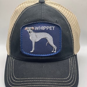 May include: Black and tan trucker hat with a navy blue patch featuring a white Whippet dog silhouette and the word "WHIPPET" in white embroidery.