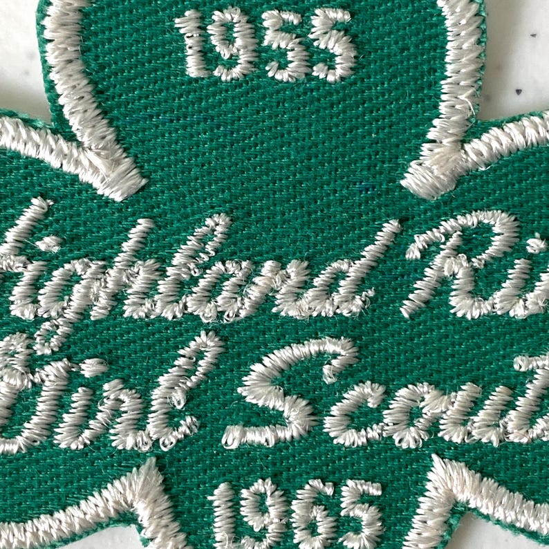 May include: A green embroidered patch in the shape of a shamrock. The patch features white stitching with the words "Highland Rim Regional Scouts" and the years "1955" and "1965".