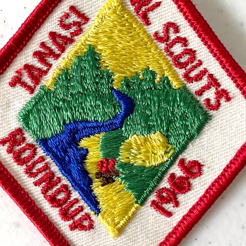 May include: Embroidered patch with a red border and the words "TANASI ROUNDUP" and "NATIONAL SCOUTS 1966". The patch features a diamond-shaped design with green trees, a blue river, and yellow and brown terrain.