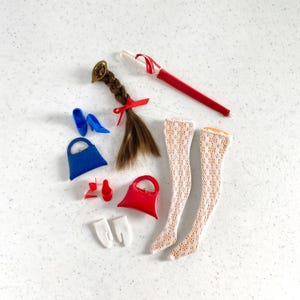 May include: A collection of miniature doll accessories, including a brown braided wig with a red bow, blue heels, a red purse, a blue purse, white gloves, red shoes, a red umbrella, and white lace stockings.