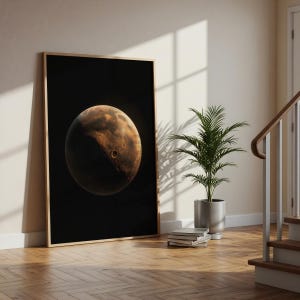May include: A rectangular wall art print in a light wood frame featuring a high-contrast depiction of the planet Mars against a solid black background. The planet displays a textured, cratered surface with shades of deep orange, brown, and black.