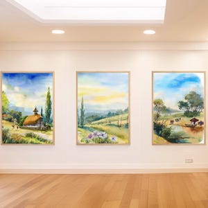 Könnte beinhalten: Drei gerahmte Aquarelle, die ländliche Landschaften darstellen. Das erste Gemälde zeigt ein kleines Häuschen mit einem Strohdach auf einem grünen Feld. Das zweite Gemälde zeigt einen gewundenen Weg durch ein Feld mit Wildblumen. Das dritte Gemälde zeigt eine Gruppe von Menschen in einem Boot auf einem See.