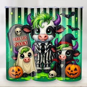 May include: A Halloween-themed tumbler featuring three cartoon cows in costumes. One is a ghost, another is dressed in a striped suit, and the third is a vampire. The tumbler has a green and white striped background with bats and pumpkins.