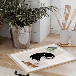 May include: A framed print with a black cat illustration on a beige background. The cat is curled up with its tail wrapped around its body. The print is surrounded by a thin wooden frame.