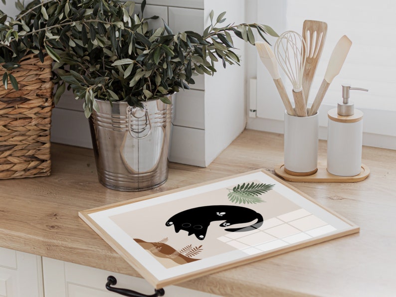 May include: A framed print with a black cat illustration on a beige background. The cat is curled up with its tail wrapped around its body. The print is surrounded by a thin wooden frame.