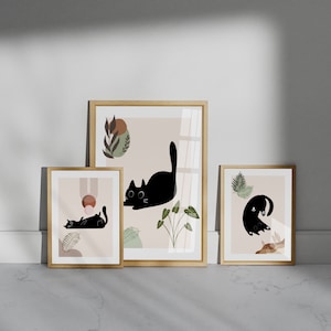 May include: Three framed prints with a minimalist design featuring black cats and abstract shapes in shades of brown, pink, and green.