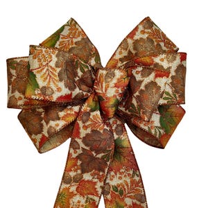 May include: A decorative bow with a fall leaf pattern in brown, orange, and green hues. The bow has multiple loops and long tails, ideal for seasonal decorations. The ribbon has a subtle shimmer, perfect for autumn.