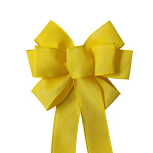 May include: A large, bright yellow bow made from a textured ribbon. The bow has two long tails.