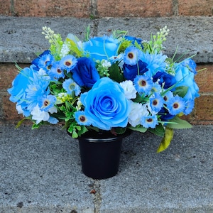May include: A blue and white artificial flower arrangement in a black pot. The arrangement features roses and smaller flowers.