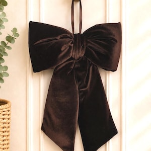 Peut inclure: Un grand nœud en velours marron foncé avec une texture douce et pelucheuse. Le nœud présente deux larges boucles horizontales et deux longs pans tombants avec des extrémités en biseau. Une fine boucle en ruban assorti est fixée au centre.