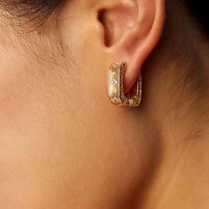 May include: A square-shaped gold hoop earring featuring a textured, brushed metal finish on the outer surface. The earring is accented with small, clear, round-cut stones embedded in a vertical row along the center of the gold band.
