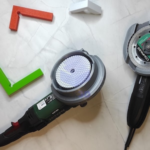 Könnte beinhalten: Zwei Winkelschleifer mit schwarzen Griffen und silbernen Köpfen, einer mit einer Schleifscheibe und der andere mit einer Trennscheibe. Ein roter und grüner Winkel und ein weißes Eckstück sind ebenfalls vorhanden.