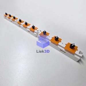 Könnte beinhalten: Eine weiße, 3D-gedruckte Schiene mit orangefarbenen Plattformen und schwarzen Knöpfen. Die Schiene ist mit gleichmäßig verteilten Löchern und Schlitzen versehen. Der Text "Liek3D" ist sichtbar.