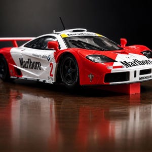 May include: A scale model race car in white and red with black wheels. The body features Marlboro branding, the number 2, Michelin logos, and Powered by BMW text. It includes a rear spoiler, a roof air intake, and a windscreen wiper on the front glass.