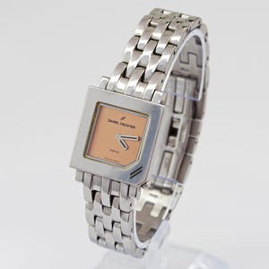 May include: A silver-toned Daniel Hechter watch with a square face and a linked bracelet. The watch face is peach-colored with black hands and the text "DANIEL HECHTER PARIS". The watch is made in France.