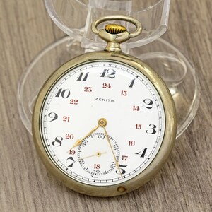 Op de afbeelding: Een vintage Zenith zakhorloge met een witte wijzerplaat, zwarte cijfers en een kleinere secondenwijzer. Het horloge heeft een goudkleurige kast en een transparante beschermhoes. Het woord "ZENITH" staat op de wijzerplaat.