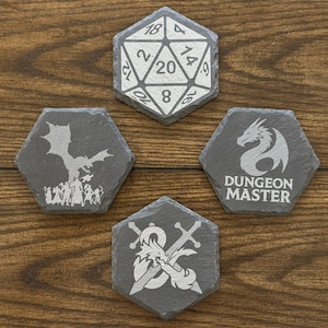 May include: A collection of five hexagonal slate coasters with white etched designs. One coaster features a 20-sided die, while others display a dragon, a dragon with crossed swords, a dragon with the words "Dungeon Master", and a dragon with a group of figures.