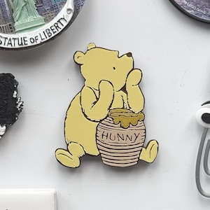 May include: A yellow cartoon bear holding a honey pot with the word "Hunny" on it. The bear is standing on a white background.