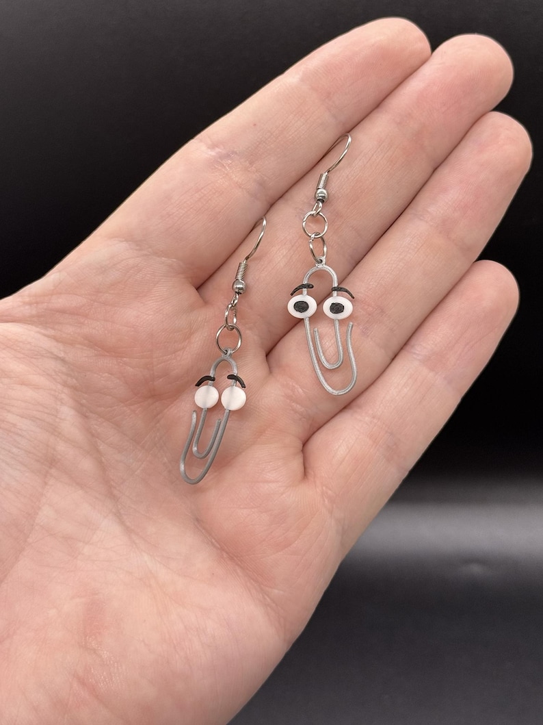 Puede incluir: Un par de pendientes originales con dise&ntilde;os de clips plateados con ojos saltones. Los pendientes tienen un cierre de gancho sencillo y se muestran sobre un fondo neutro.