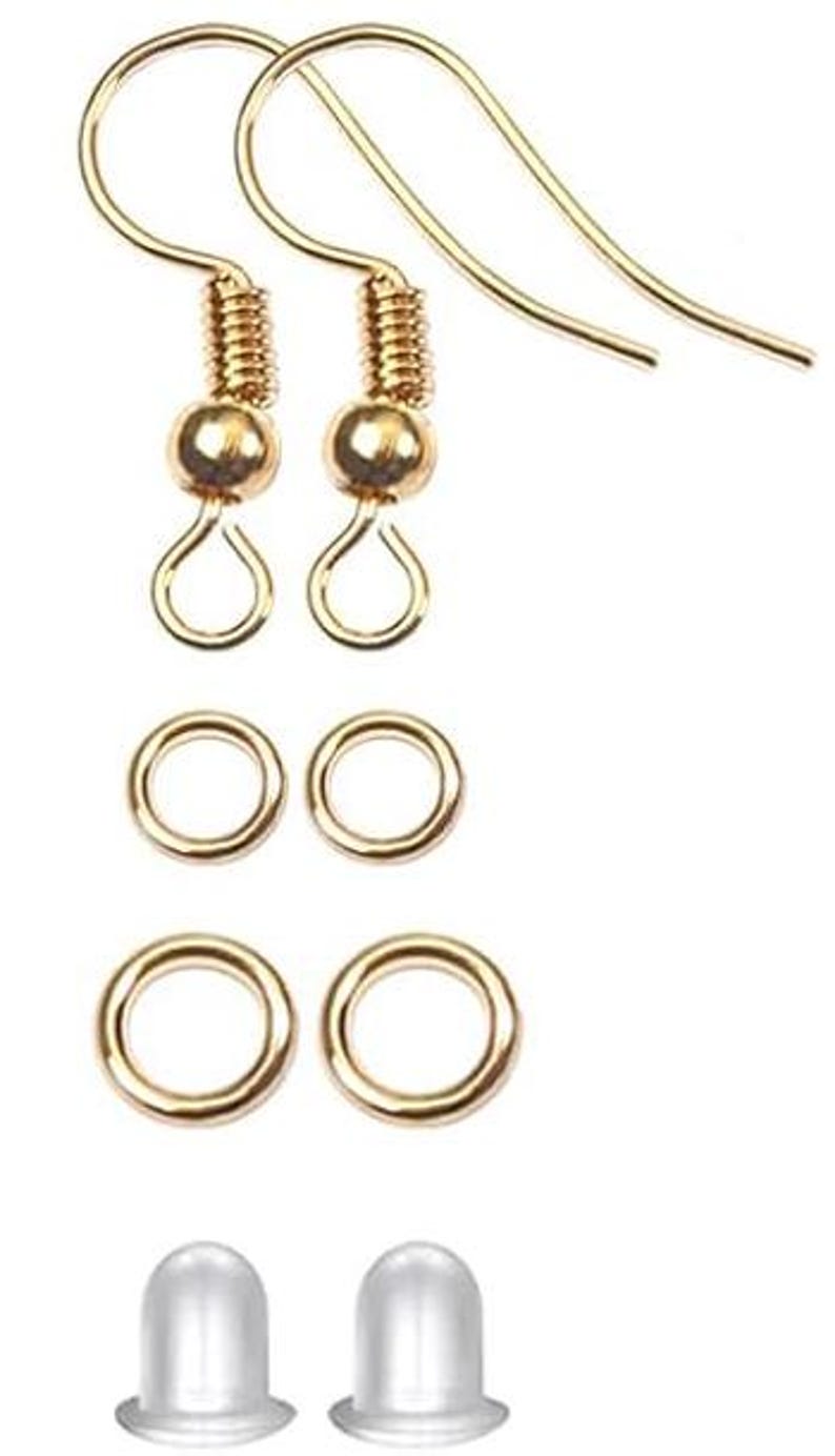 Puede incluir: Un conjunto de componentes de pendientes dorados, que incluyen dos ganchos para pendientes, dos peque&ntilde;as cuentas redondas, dos anillas, dos anillas m&aacute;s grandes y dos topes transparentes. Los componentes est&aacute;n dispuestos sobre un fondo blanco.