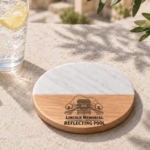May include: A round coaster featuring a split design of white marble and light brown wood. The wooden section displays a black line art illustration of the Lincoln Memorial and Reflecting Pool with the text LINCOLN MEMORIAL REFLECTING POOL.
