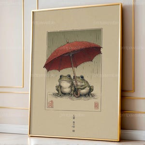 以下が含まれることがあります： 雨の中で赤い傘の下にいる2匹のカエルを描いた額入りのアートプリント。このアートワークは、柔らかい色と詳細な線画を備えた、ヴィンテージの日本の美学を持っています。プリントは金のフレームに入っています。