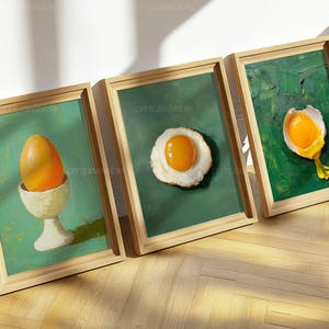 Può includere: Tre stampe artistiche incorniciate con dipinti a tema uova. Uno mostra un uovo intero in un portauovo, un altro un uovo fritto e il terzo un uovo rotto. I dipinti hanno uno sfondo verde e sono in cornici di legno.