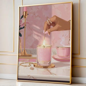 May include: Framed art print showing a hand lighting a pink candle. A teacup, saucer, and jewellery are also present. The color palette is dominated by pink and gold tones, creating a luxurious and relaxing atmosphere.