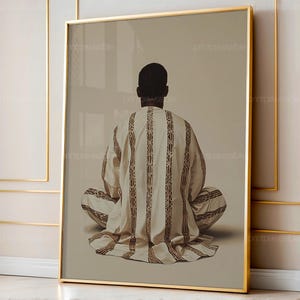 May include: A framed print featuring a person in traditional attire, viewed from the back. The person is seated with legs crossed, wearing a cream-colored garment with vertical brown stripes. The artwork is set against a neutral background.