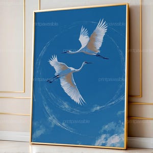 Pode incluir: Uma impressão de arte emoldurada com duas garças brancas em voo contra um céu azul. As aves são retratadas com as asas abertas, e a obra de arte tem um estilo minimalista. A moldura é dourada.