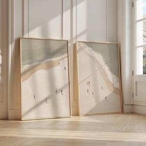 Pode incluir: Duas impressões de arte emolduradas retratando uma cena de praia com figuras minimalistas. A obra apresenta uma praia arenosa, ondas do oceano e uma paleta de cores suaves bege, castanho e cinza. As molduras são de cor de madeira clara.
