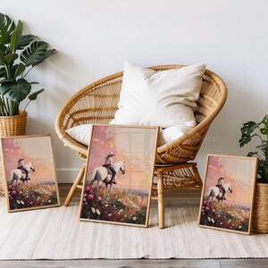 May include: Three framed art prints depicting a cowboy on a white horse in a wildflower meadow at sunset. The prints are in wooden frames and are displayed near a wicker chair and potted plants. The colour scheme includes pinks, oranges, and greens.