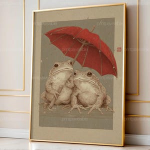 以下が含まれることがあります： 赤い傘の下にいる2匹のカエルが描かれた、額装されたアートプリント。ヴィンテージな雰囲気です。アートワークはセピア色で、カエルと傘が焦点となっています。プリントは金のフレームに入っています。