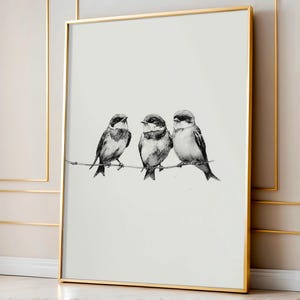May include: A framed art print featuring three detailed black and white bird illustrations perched on a thin branch. The birds have dark markings around their eyes and are set against a white background. The frame is gold.