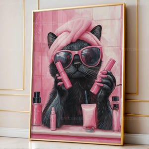 Può includere: Stampa incorniciata raffigurante un gatto nero con occhiali da sole rosa e un asciugamano in testa, che tiene in mano trucchi rosa. Il gatto è circondato da vari prodotti cosmetici rosa, su uno sfondo piastrellato rosa.