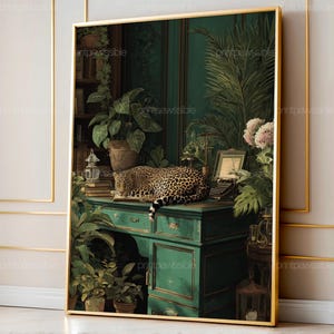 Può includere: Stampa incorniciata con un leopardo che riposa su una scrivania verde acqua, circondato da vegetazione lussureggiante e una macchina da scrivere vintage. L'opera d'arte ha una cornice dorata ed evoca un tema classico e botanico.