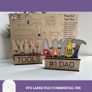 Puede incluir: Un kit de caja de herramientas Pop Out de madera con las palabras "TOOLS" y "#1 DAD" mostradas. El kit incluye varias formas de herramientas, como una sierra, unos alicates y un martillo, con instrucciones en el lateral. El kit es un archivo láser SVG para uso comercial.