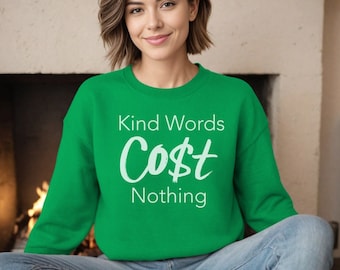 May include: A vibrant green sweatshirt featuring the text "Kind Words Cost Nothing" in white. The crew neck sweatshirt is worn by a person, with the words clearly displayed.