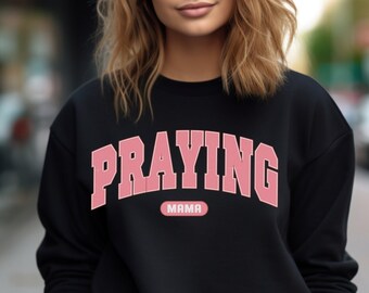 May include: Black sweatshirt with a pink "Praying Mama" graphic. The text is in a collegiate font.