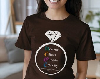 May include: A brown t-shirt with a diamond ring design and the words "Heaven Offers People Eternity" arranged in a circle. The shirt also features the Bible verse John 14:19. The person in the image is smiling.