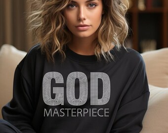 May include: A black sweatshirt with the word "GOD" and the word "MASTERPIECE" in a rhinestone design. The sweatshirt is worn by a person sitting on a beige sofa.