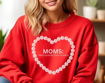 May include: Red sweatshirt featuring a heart-shaped design made of pink pearls. The heart contains the text "MOMS: PRECIOUS BEYOND PEARLS" inside.