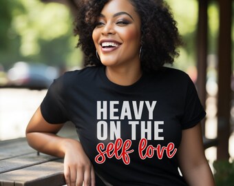 May include: A black t-shirt with white text that reads "Heavy on the self love" in red cursive lettering.