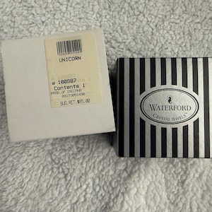 May include: A white box with black text that reads "UNICORN 100887 Contents 1 PROD. OF IRELAND 09173051430 SUG.RET. $85.00" and a black and white striped box with the text "WATERFORD CRYSTAL JEWELS".